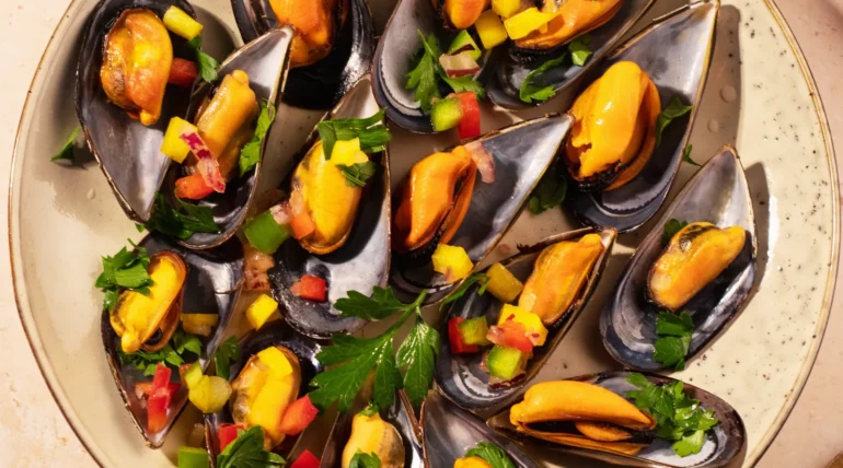 Plato de mejillones al vapor con salsa de mango y pimientos, decorado con perejil fresco. Ideal para una comida gourmet o aperitivo.